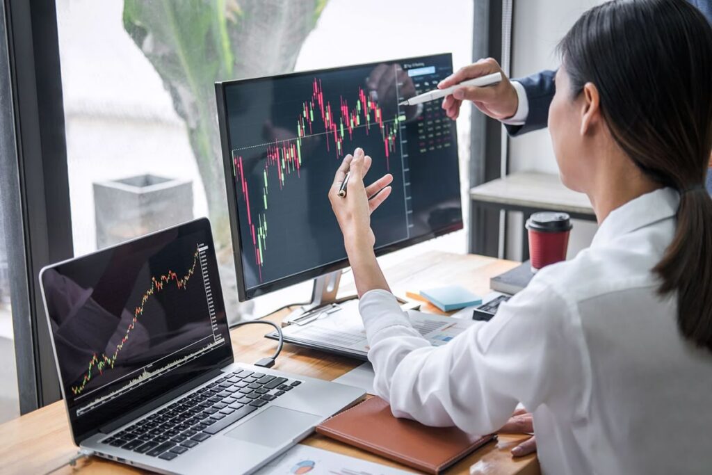 Zwei Finanzexperten analysieren Aktienkurse auf Monitoren und besprechen Strategien, was die Chancen und Risiken von Investitionen im Ausland veranschaulicht.